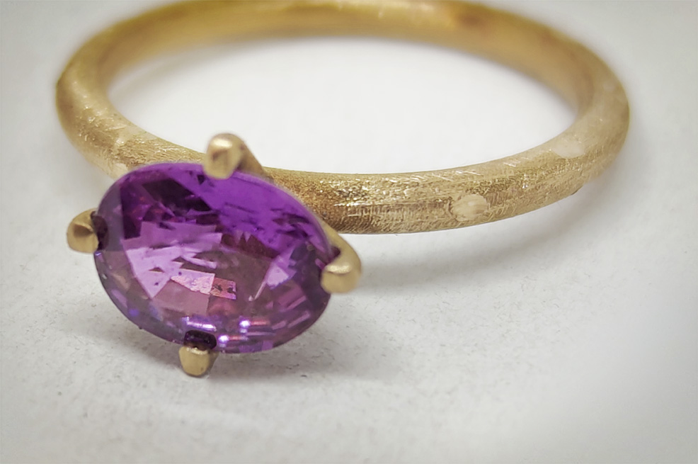 Dettaglio delle sfaccettature di uno zaffiro viola montato su un anello in oro grezzo